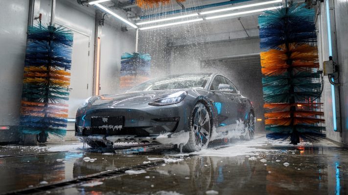 Visualisiert das Kernthema direkt: E-Auto in der Waschanlage, modernes Setting und typische Waschstraßen-Umgebung.