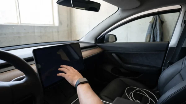 Eine Hand mit Smartwatch berührt den großen zentralen Bildschirm im Innenraum eines Autos.